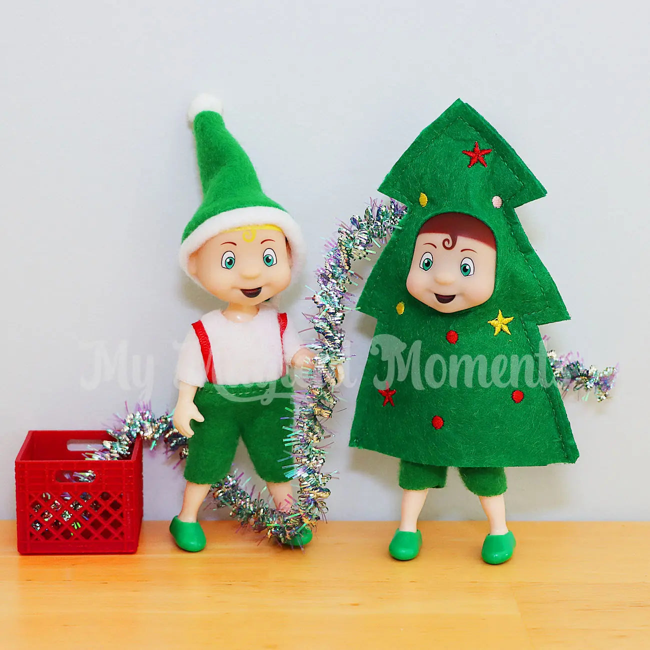 Elf toddler wearing a tree costume being decorated by a blonde hair toddler elf