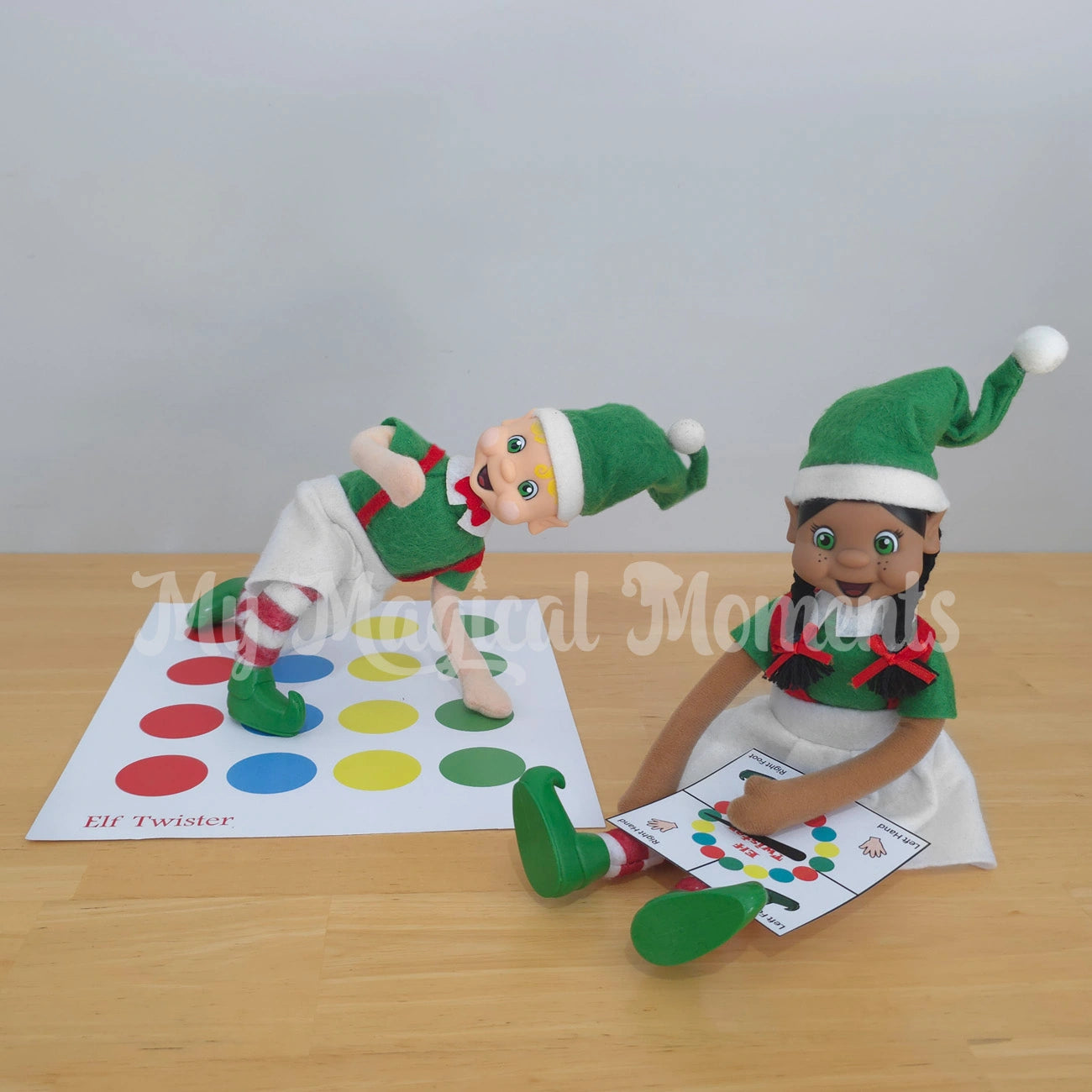 Elves playing a game of twister, blonde hair boy is bendable and has one foot on blue and one on red, his hand is on green. A black hair girl with bows is playing with the spinner