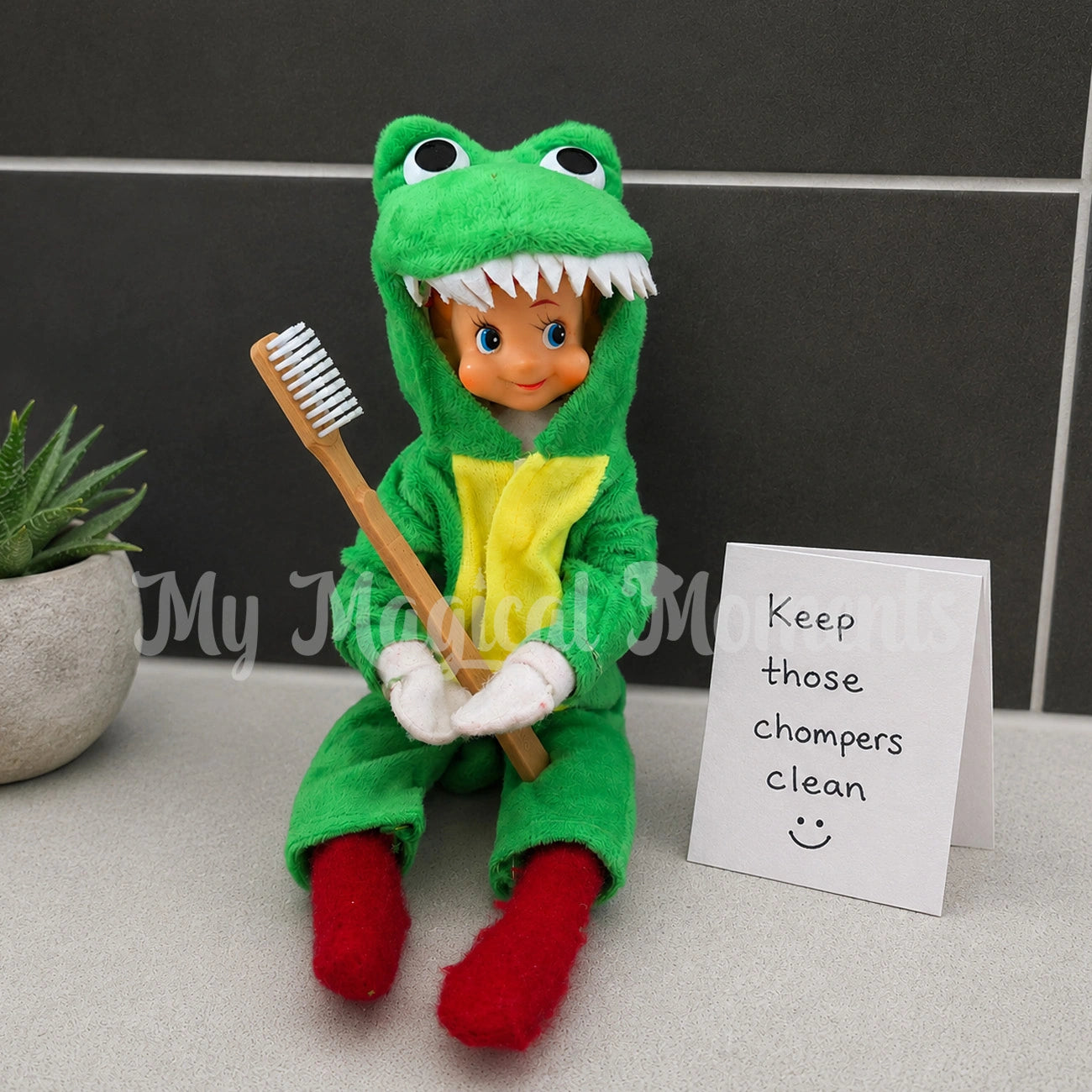 Elf wearing a crocodile costume, holding a tooth brush, with a note saying Keep those chompers clean