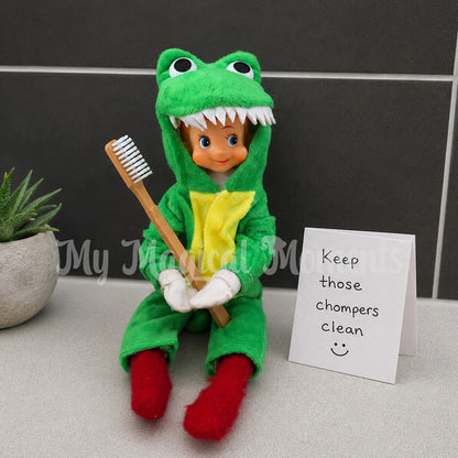 Elf wearing a crocodile costume, holding a tooth brush, with a note saying Keep those chompers clean