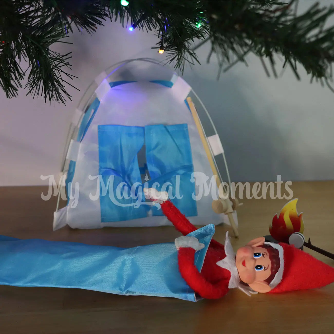 Elf sleeping under the Christmas tree with a mini sleeping bag and tent