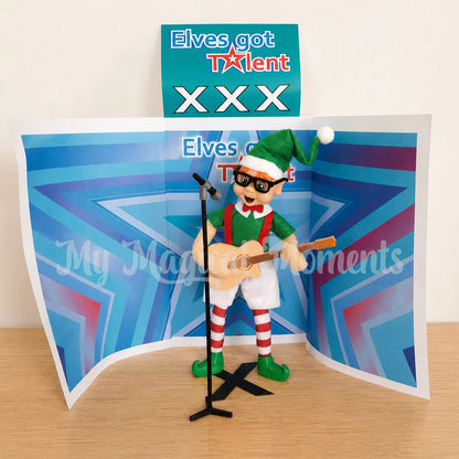 Elf wearing glasses looking like ed sheeran playing a guitar prop singing into a microphone with a stage that says elves got talent