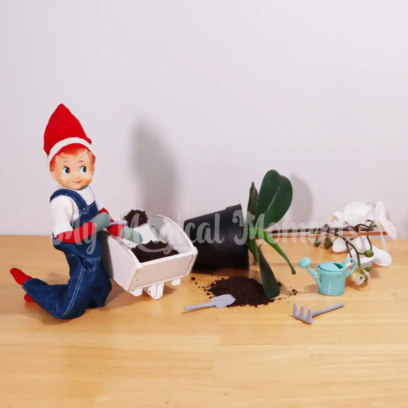 Elf wearing overalls putting oreo cookie dirt in a wooden elf wheel barrow with gardening tools