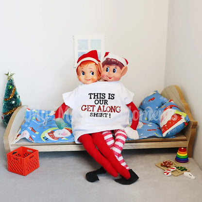 Elves wearing a get along shirt on a mini wooden bed with elf props