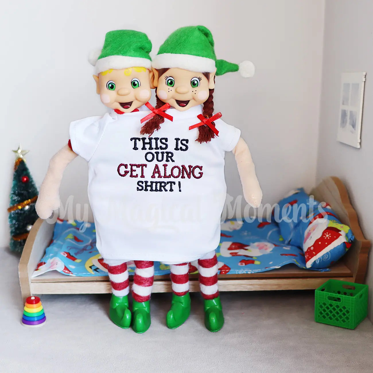 Brown hair Girl elf and a blonde hair boy elf standing in a get along shirt in front a mini bed scene