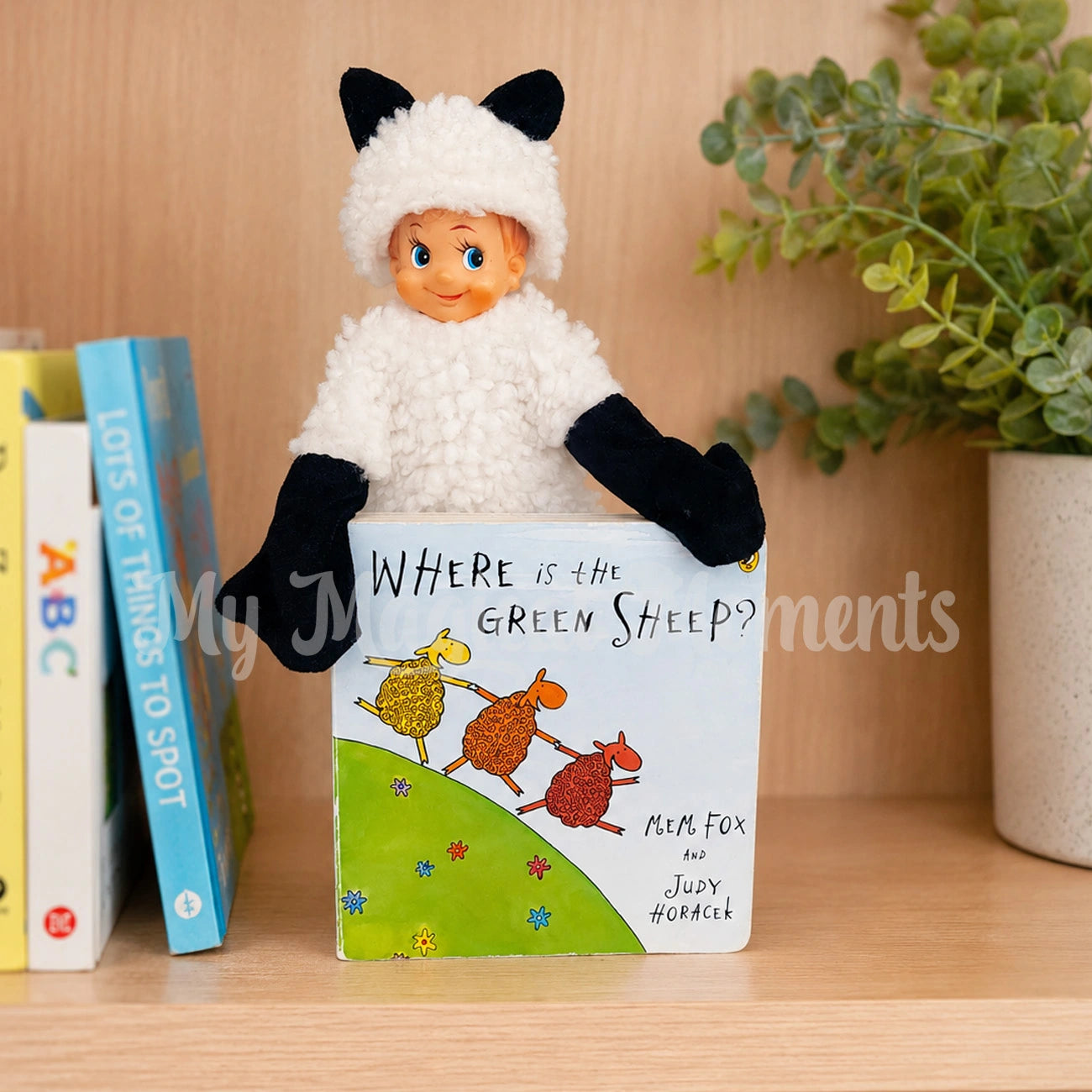Elf wearing a sheep costume, on a book shelf with Where is the Green sheep book