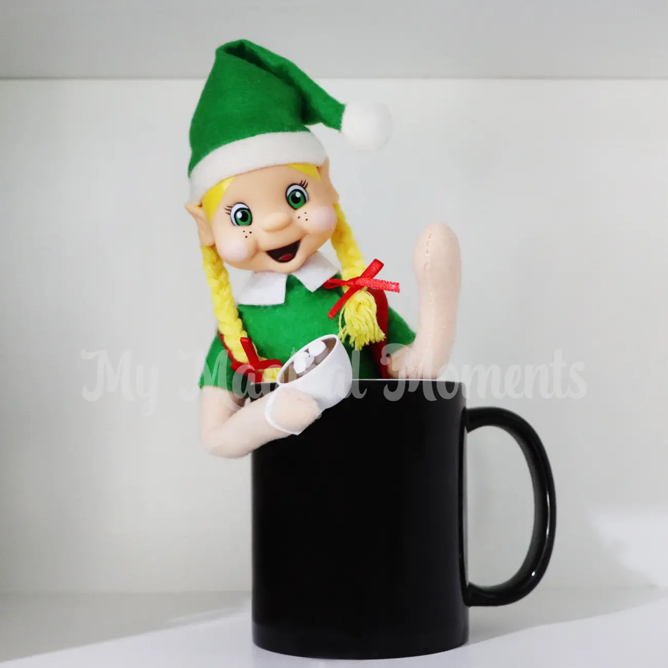 elf sitting in a mug with mini hot chocolate