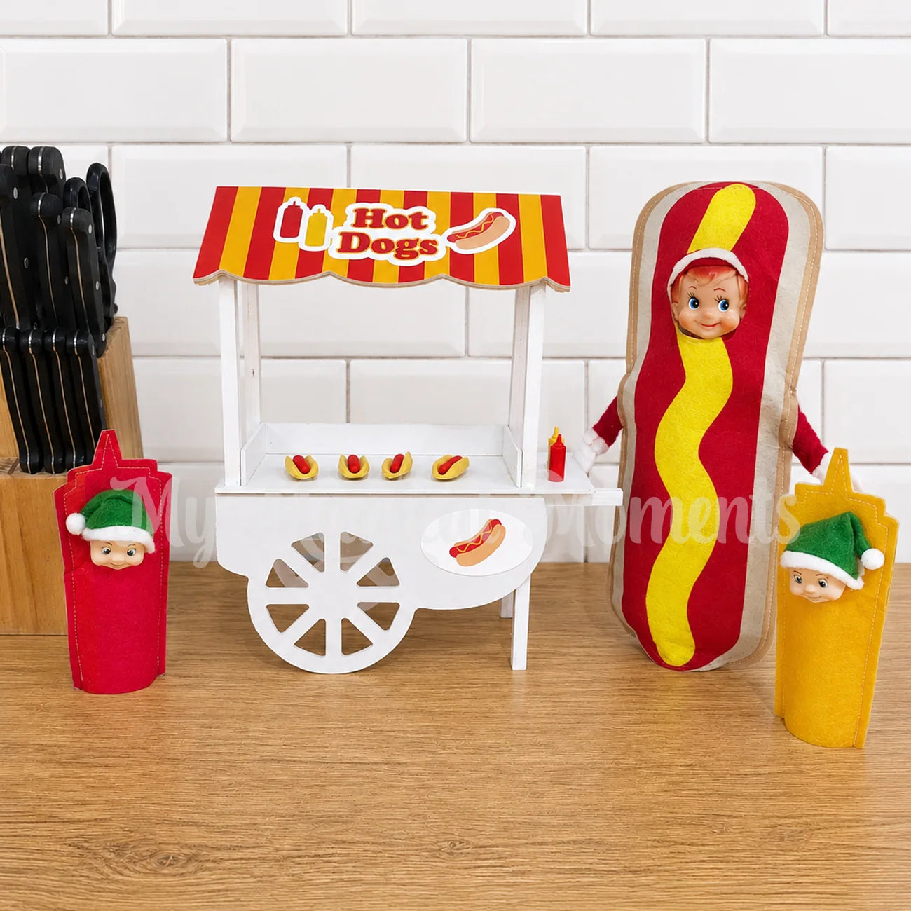Elf wearing a hot dog costume, selling hot dogs from a hot dog stand, with elf toddlers dressed as sauces