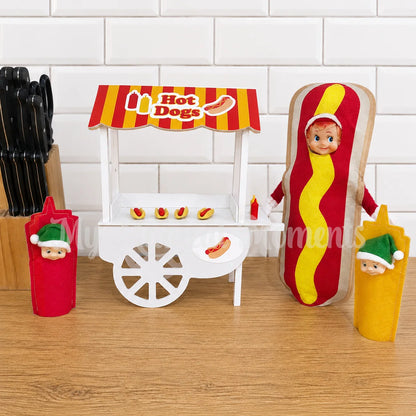Elf wearing a hot dog costume, selling hot dogs from a hot dog stand, with elf toddlers dressed as sauces