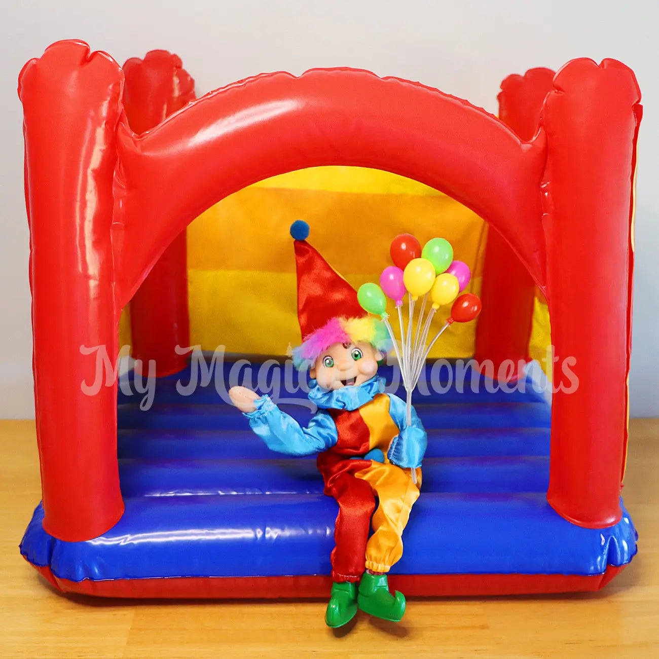 Elf wearing a clown costume holding balloons on a jumping castle