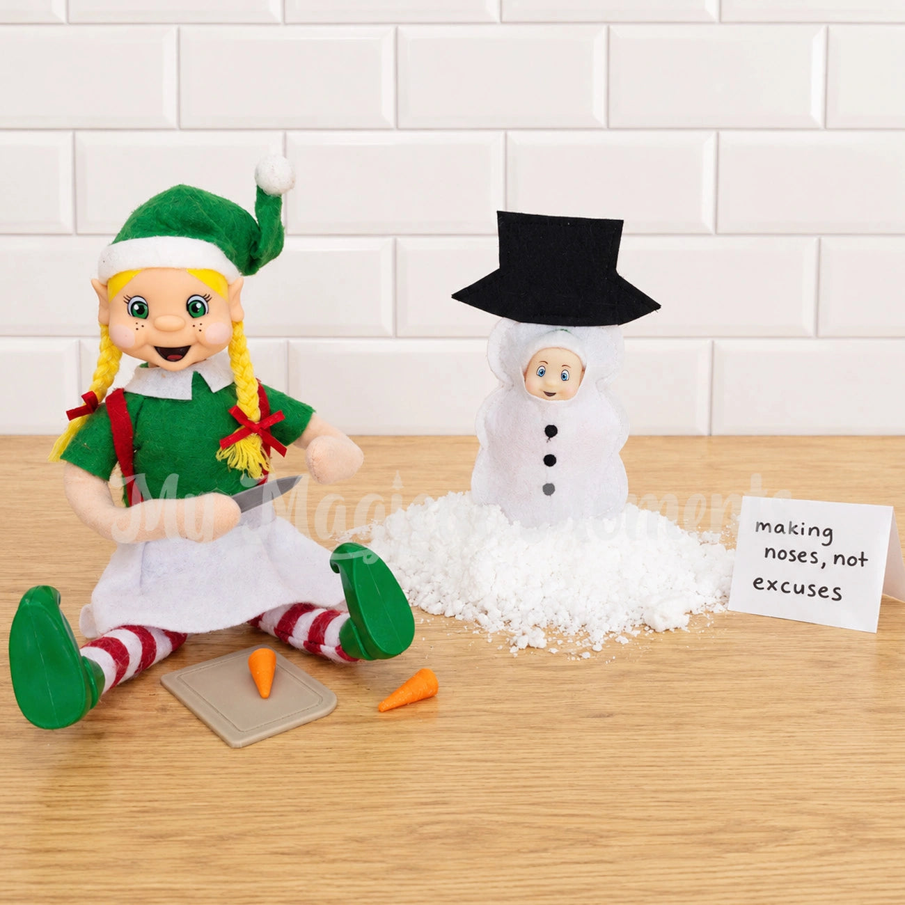 A blonde hair elf, cutting mini carrots on a chopping board, for a baby elf dressed as a snowman with a note