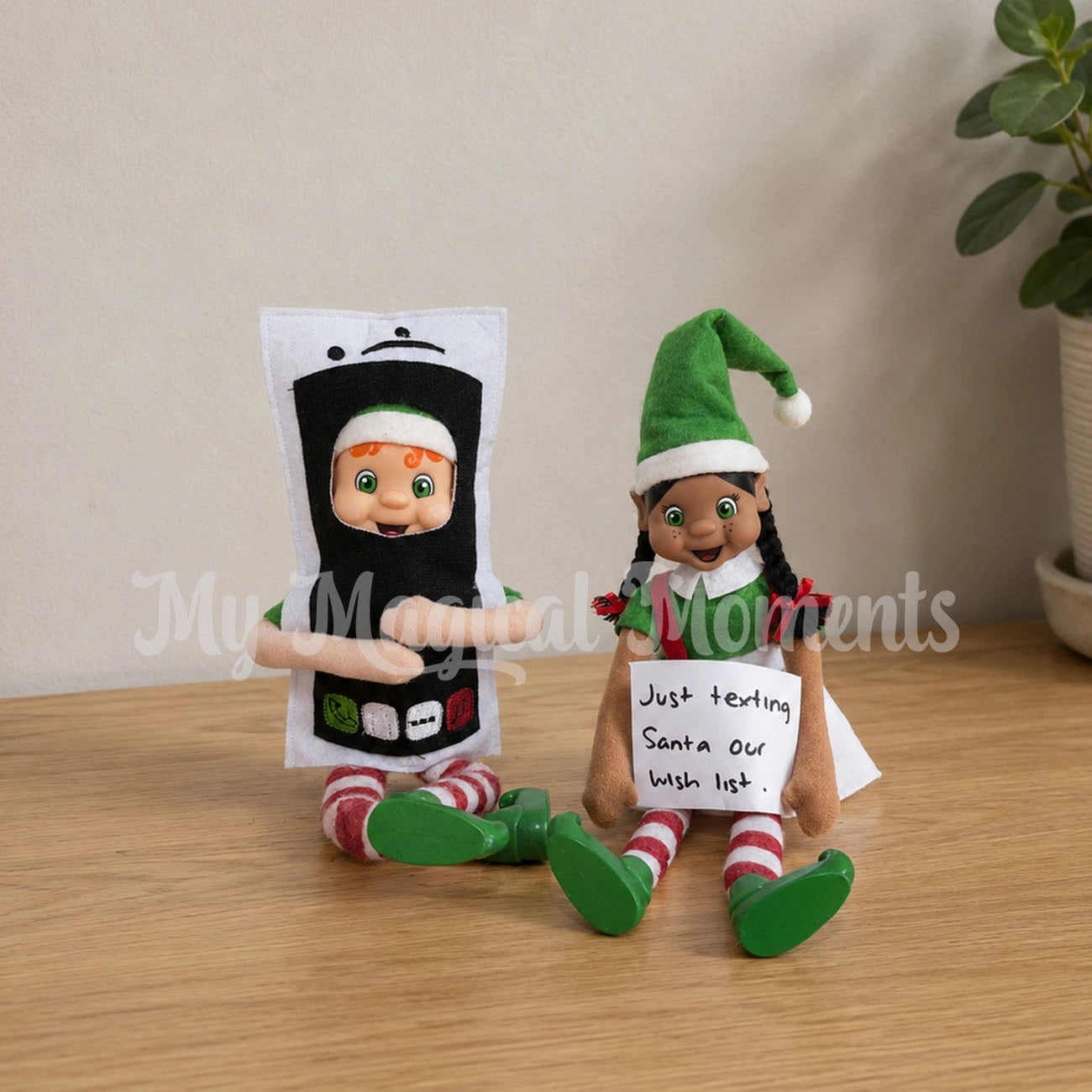orange hair bendable elf wearing a mobile phone costume, texting Santa, with a black hair elf holding a sign that says, Just Texting Santa our wish list