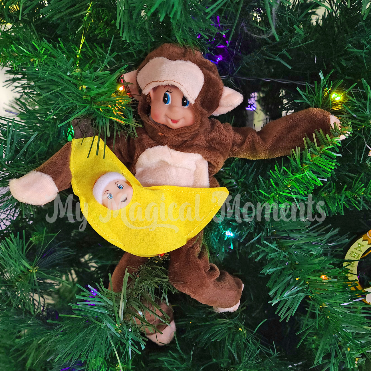 Elf dressed as a monkey in a christmas tree holding a baby elf dressed in a banana costume