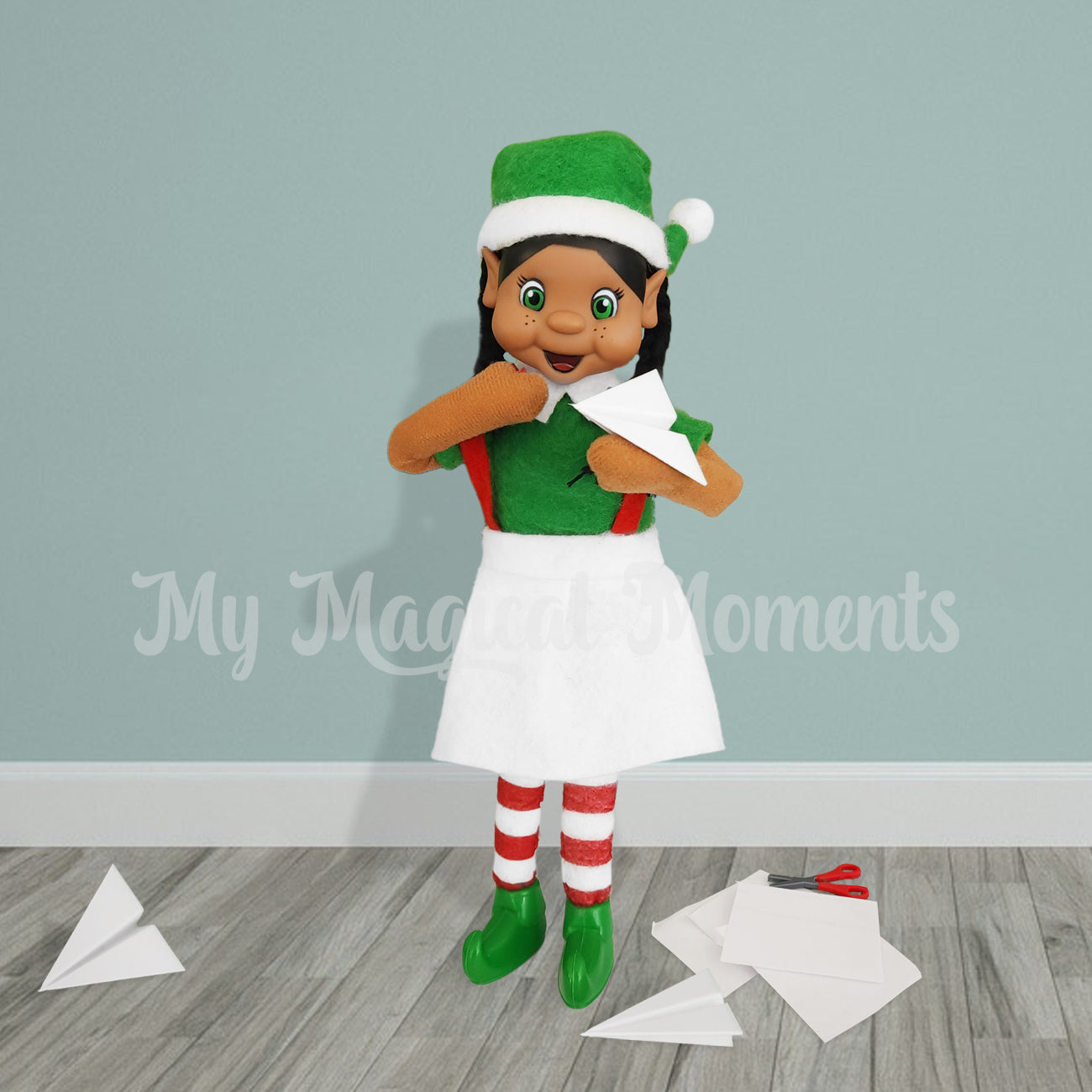 An elf scene with my elf friends black haired girl, holding a paper airplane prop. With paper and miniature scissors on the floor.