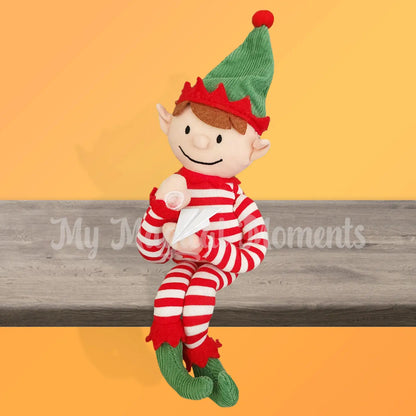 An elf for Christmas elf sitting on a shelf with a paper airplane elf prop