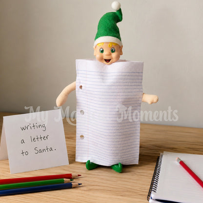 Blonde hair elf dressed in a paper costume, on a table with papers and pencils. There is a sign that says writing a letter to Santa