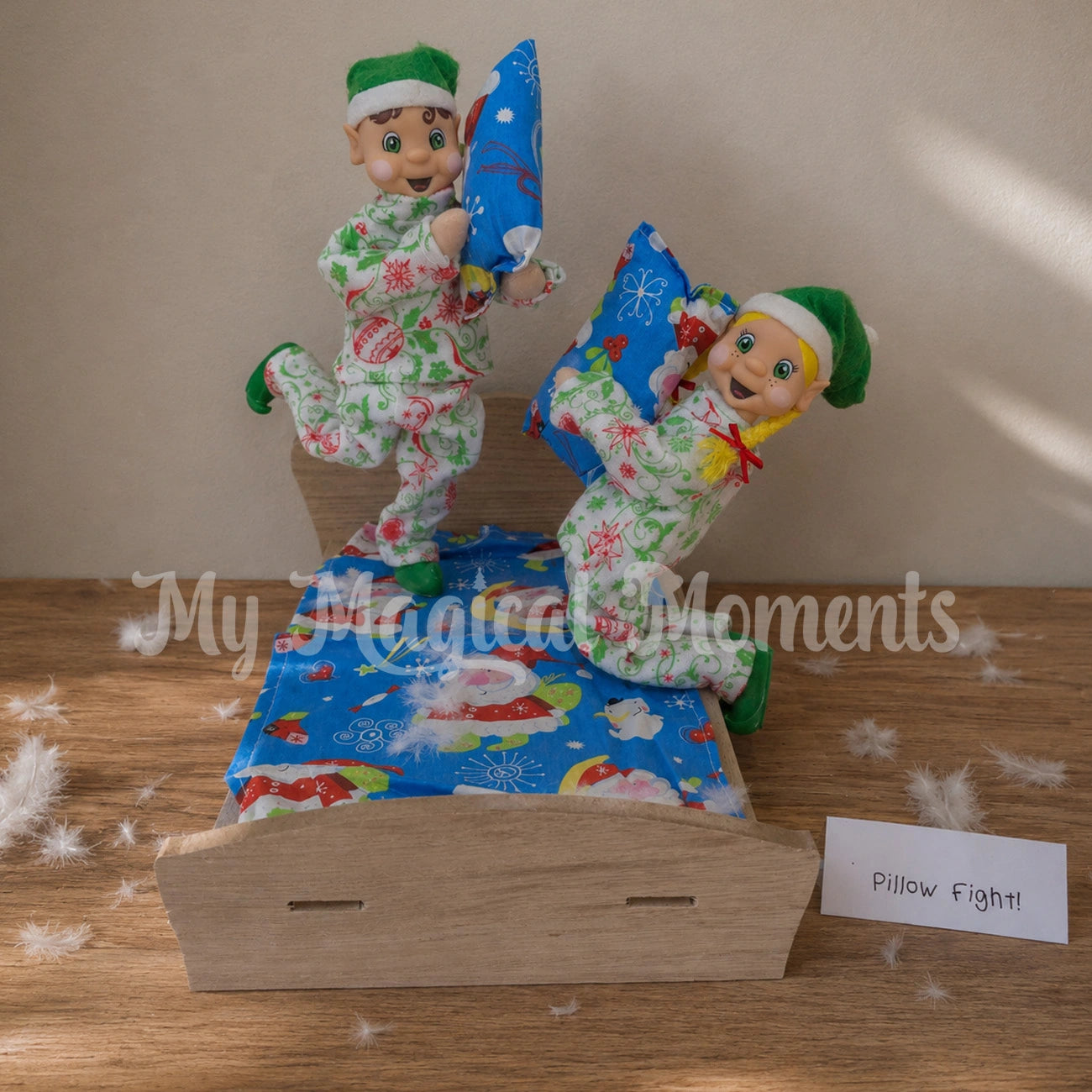 Brown Hair Elf wearing ornament patterned Pyjamas, having a pillow fight with a blonde hair girl wearing christmas Pjs. Both on a wooden bed with feathers around. 