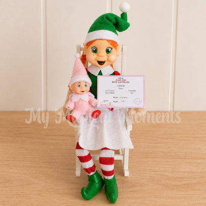 Baby Elf wearing a pink outfit being held by an orange hair girl elf sitting on a rocking chair and a baby elf birth certificate