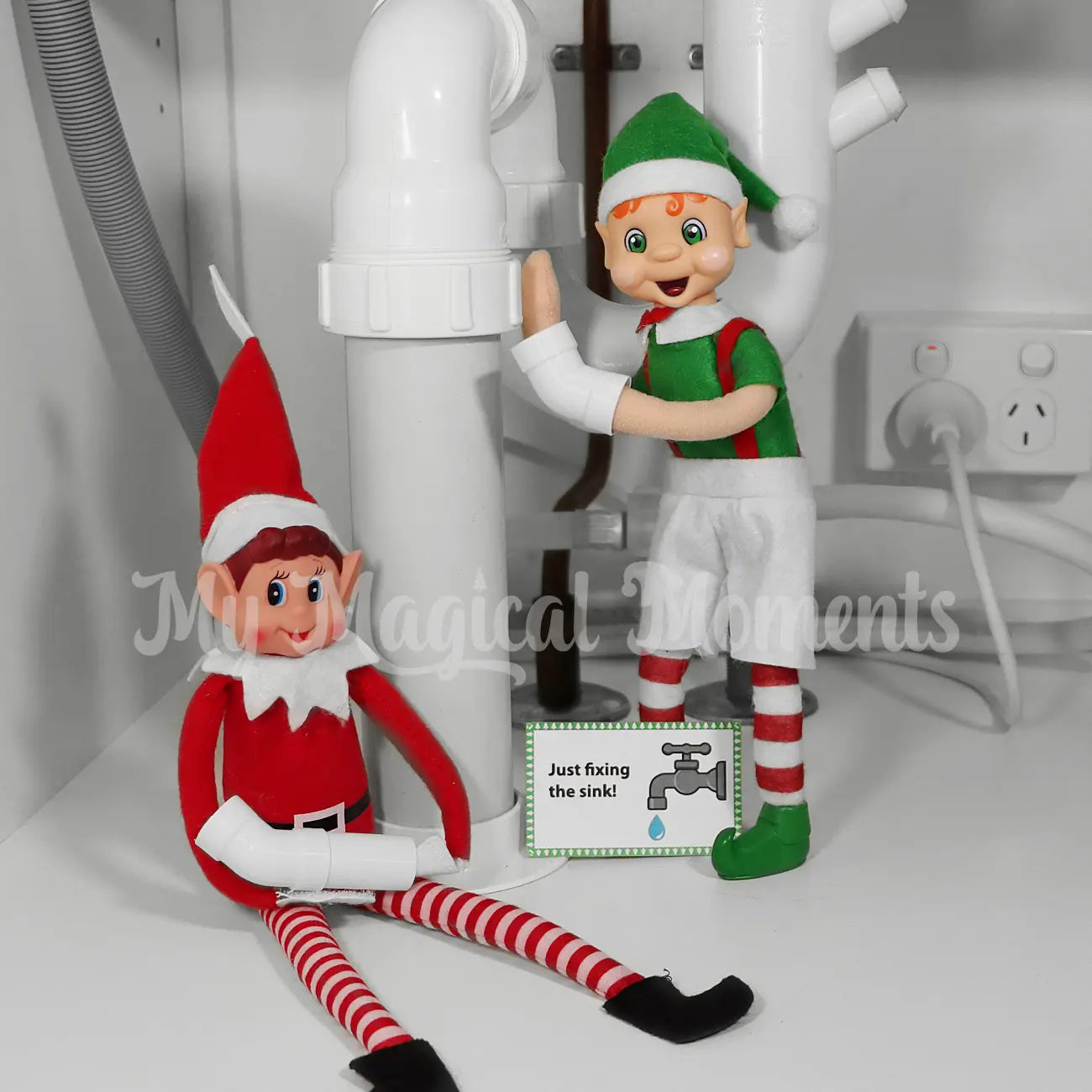 Two elf dolls in red and green outfits with a sign indicating they are fixing a sink.