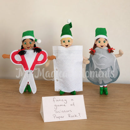 Elves wearing Scissors costume, Paper costume and a rock costume. There is a handwritten sign that says fancy a game of scissors paper rock