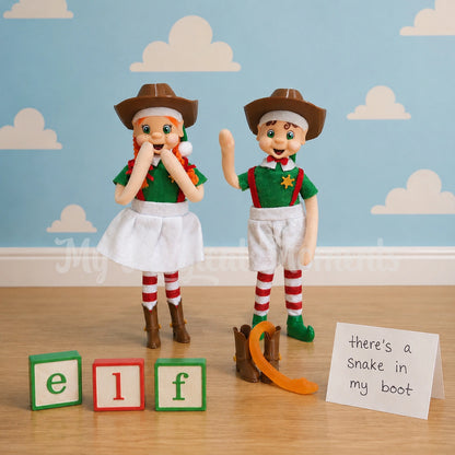 a orange hair bendable elf standing wearing a cowboy hat and boots, a brown hair boy elf standing waving wearing a cowboy hat and sheriff badge, there is two cowboy boots on the ground and a snake coming out of it . the sign says there's a snake in my boot