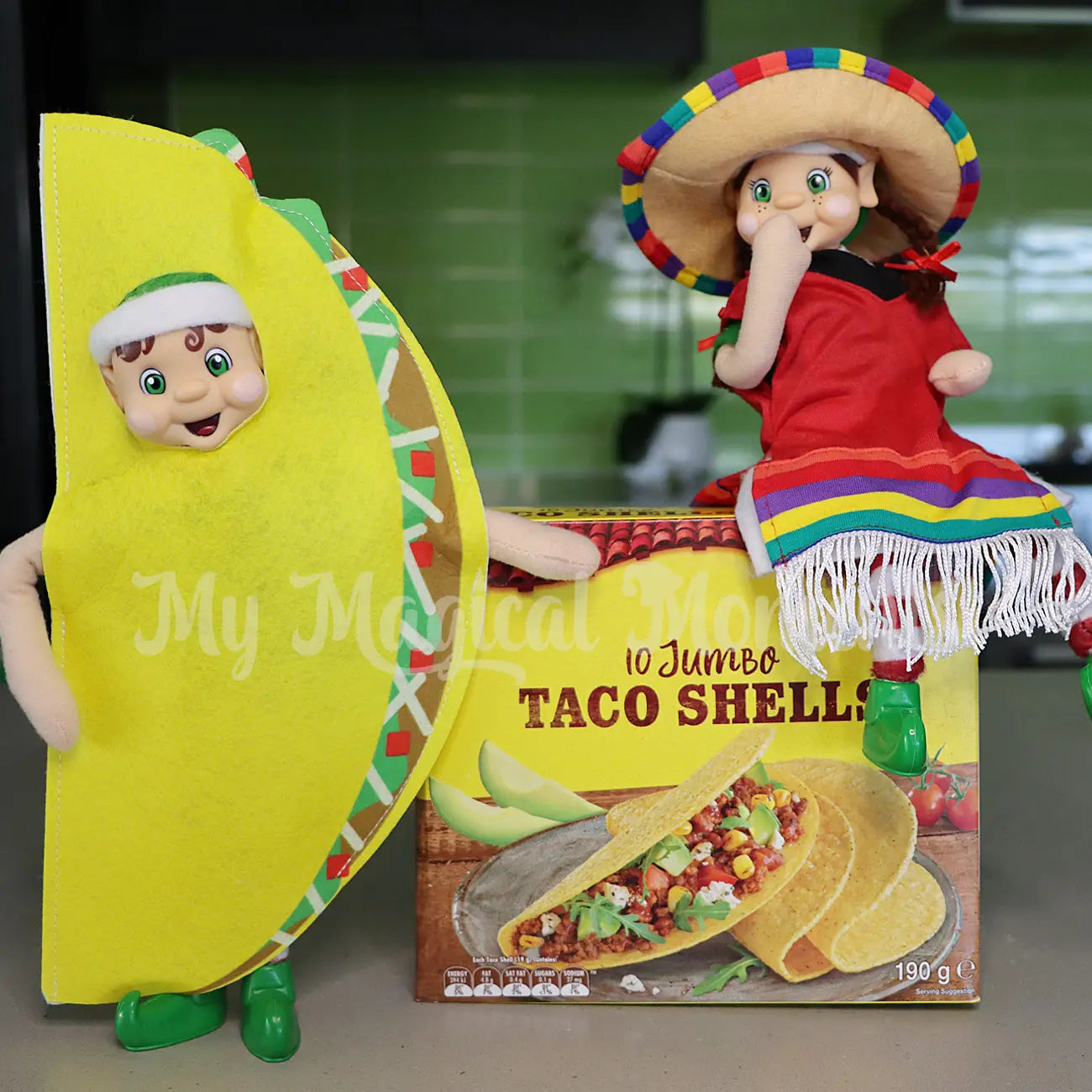 Elves dressed as a taco and in a Mexican costume sitting on a box of tacos