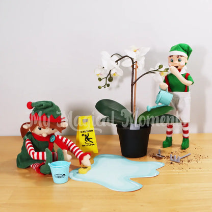 Elf For Christmas cleaning a spill with a bucket and mini sponge made by a brown hair boy My Elf Friends standing watering a plant. There is gardening tools and a caution wet floor sign