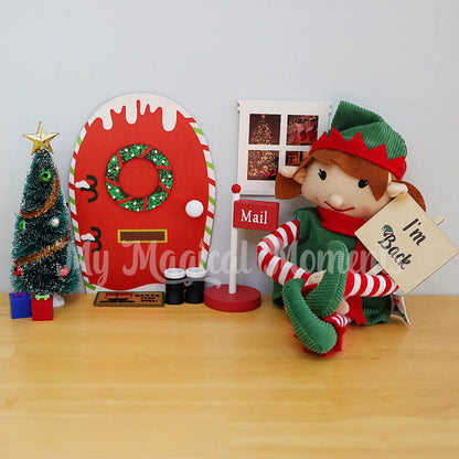 Elf arriving with an im back sign by their elf door with Chrismtas tree, presents door mat and mailbox