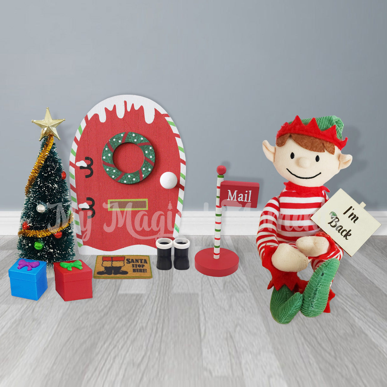 an elf holding an I'm back sign next to an elf door, christmas tree and miniature elf accessories