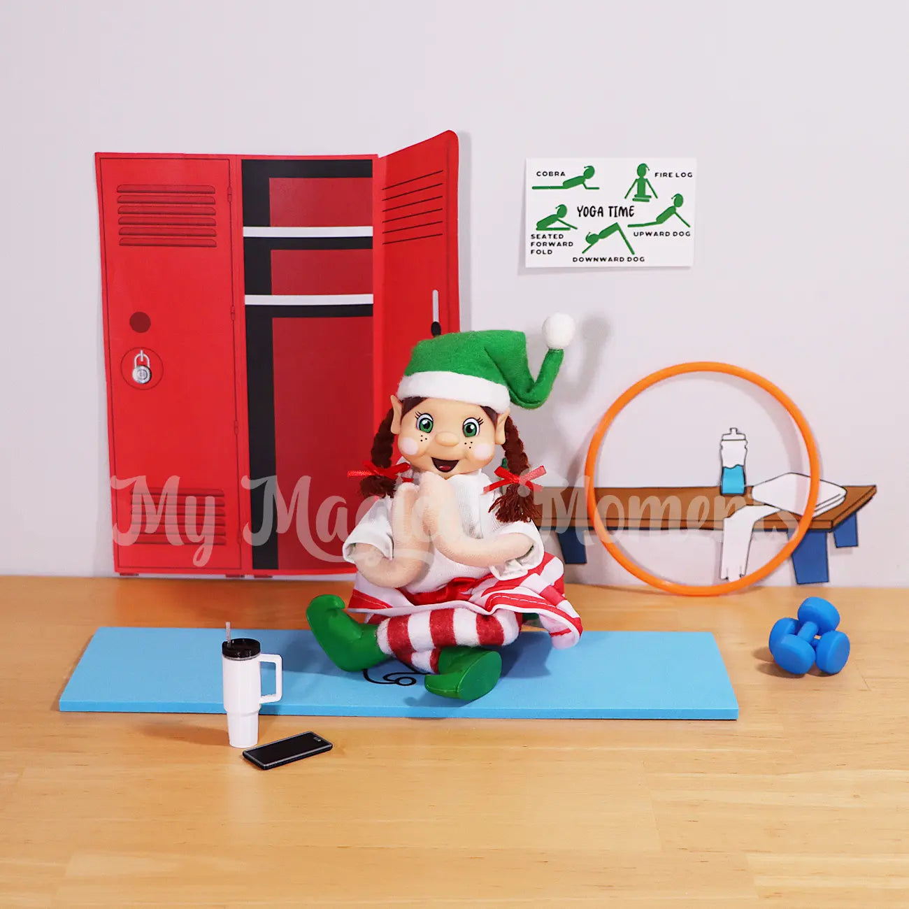 Brown Hair Bendable elf friends wearing a white shirt, a skirt doing a yoga pose sitting on a blue yoga mat. In a gym with a hula hoop, mini stanley cup, elf mobile phone and dumbbells