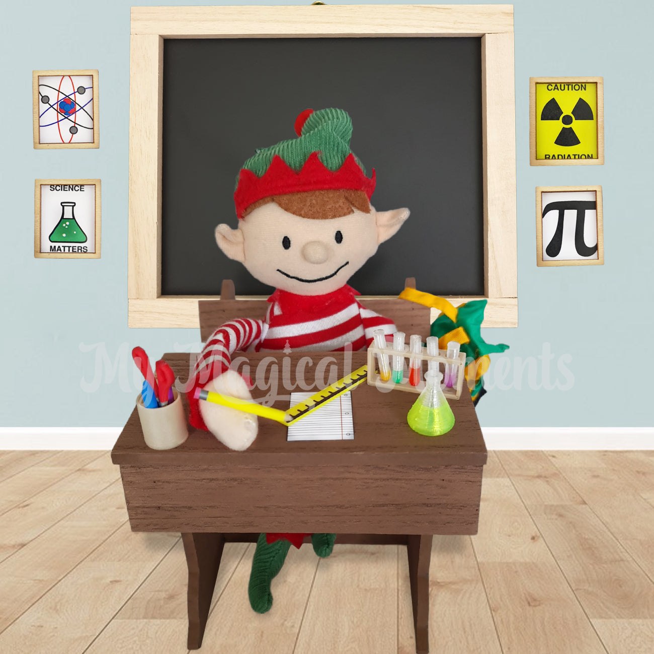 Elf For Christmas sitting at a school Desk, with a chemistry set, stationery and chalkboard behind the elf