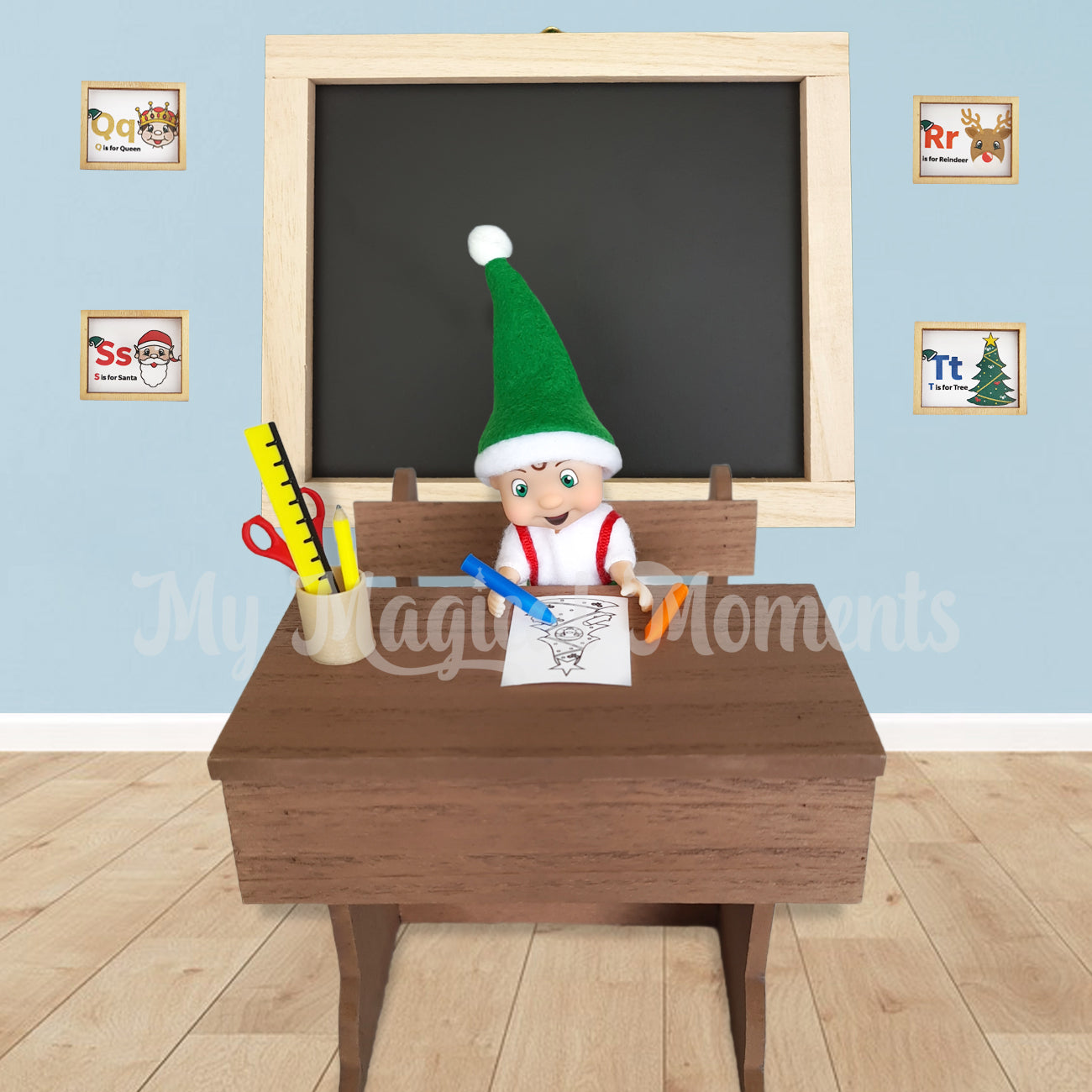 Elf toddler colouring on an elf sized school desk with crayons and miniature stationery. There is a chalkboard behind
