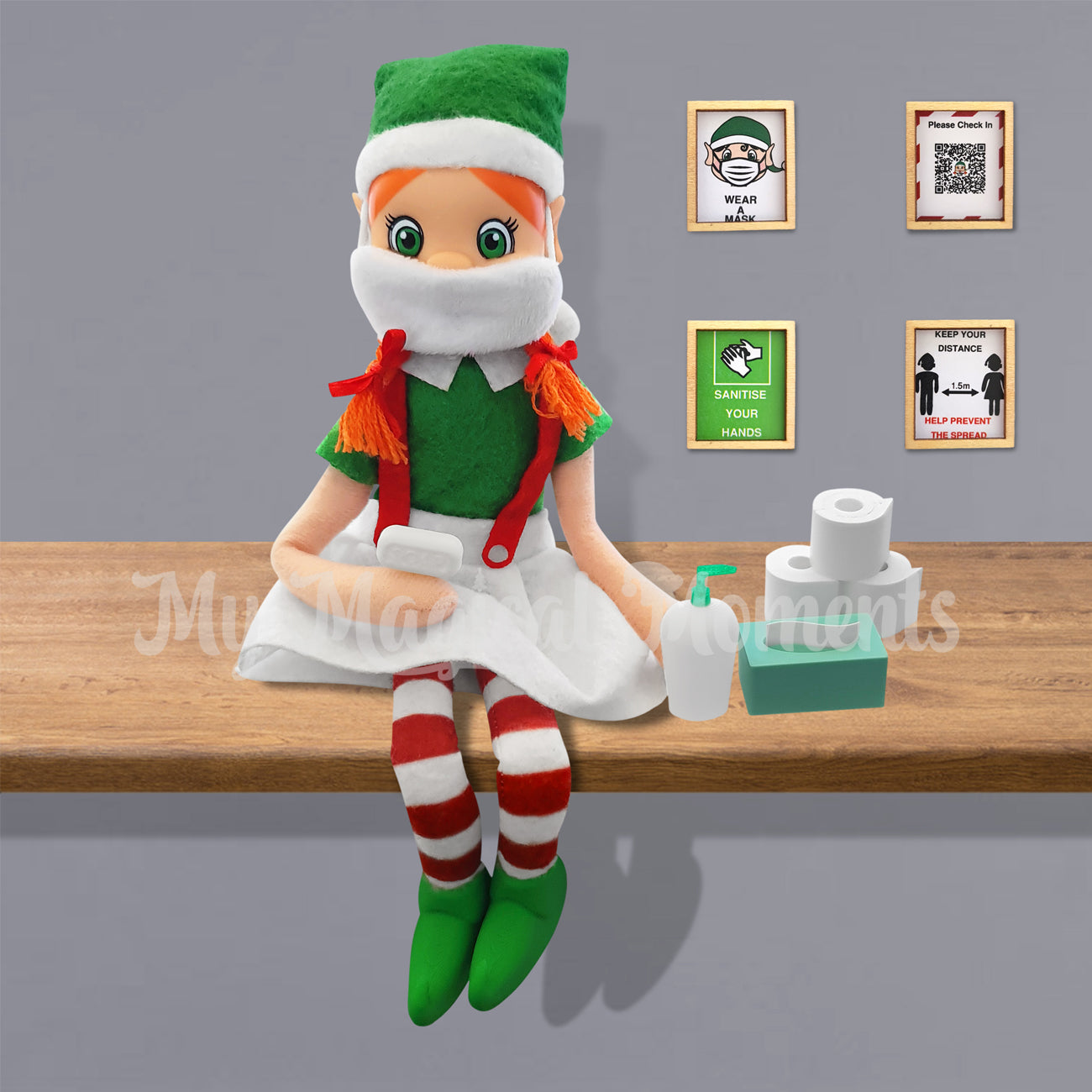 Orange hair elf wearing a tiny face mask holding soap on a shelf. Next to her is elf sized toilet paper, tissues and santiser